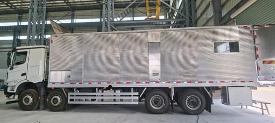 Side view of a truck-mounted QR-GT1800 generator enclosure in an assembly hall