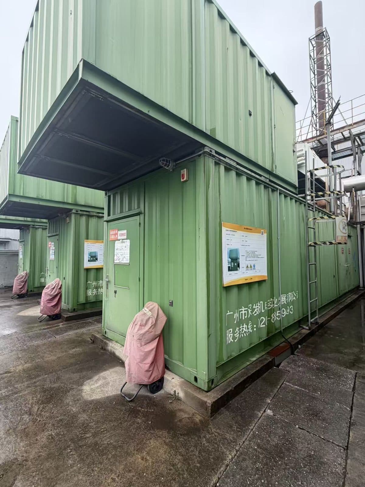 Green containerised generating sets in a row, exterior, with access doors and fire extinguishers